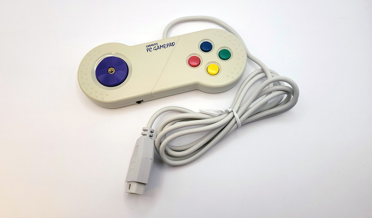 A photograph of a beige Gravis Gamepad, with a purple D-pad and four multicolored face buttons.