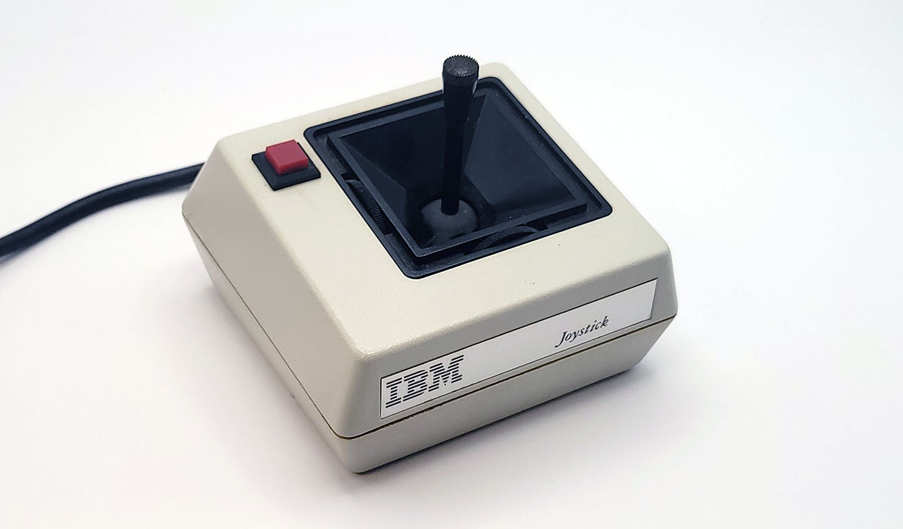 A photograph of a beige IBM PCjr joystick, with a black, square pyramidal well where the stick can be moved around on two independent axes.